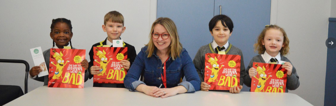Michelle is holding a pen and smiling for the camera. Four happy school children stand beside her holding signed copies of The Day The Banana Went Bad.